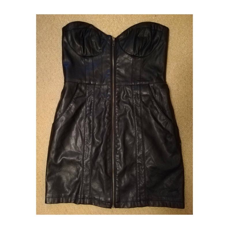 May include: A black strapless faux leather dress with a front zipper closure and two pockets. The dress has a fitted bodice and a slightly flared skirt.