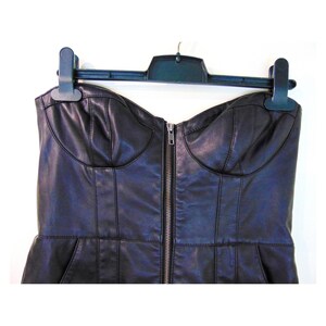 May include: A black strapless faux leather dress with a zipper down the front. The dress has a fitted bodice and a slightly flared skirt.