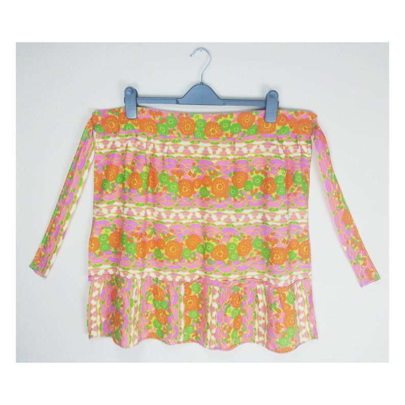 May include: A vintage apron with a floral print in shades of orange, pink, green, and yellow. The apron has a ruffled hem and ties at the waist.