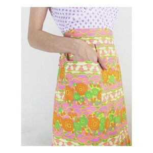 May include: A pink, orange, and green floral print dress with a white pocket. The dress has a white background with a pink, orange, and green floral pattern. The dress has a white pocket on the right side.