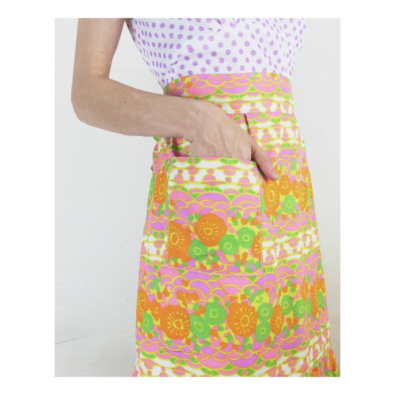 May include: A pink, orange, and green floral print dress with a white pocket. The dress has a white background with a pink, orange, and green floral pattern. The dress has a white pocket on the right side.