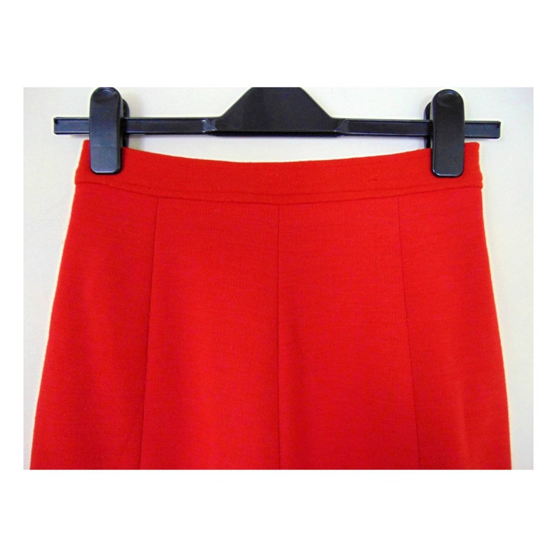 May include: A bright red skirt with a high waist and a straight cut. The skirt is hanging on a black hanger.