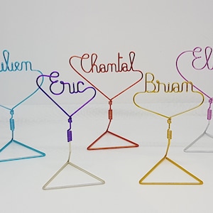 Peut inclure: Cinq porte-noms en forme de cœur en fil de fer de différentes couleurs. Les noms sont Julien, Eric, Chantal, Brian et Elise.