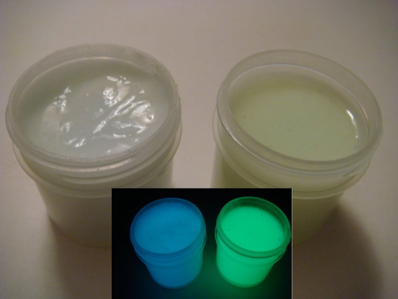 May include: Two white plastic jars of glow-in-the-dark paint. The jars are sitting on a white surface. The paint in the jars is white, but it glows blue and green in the dark.