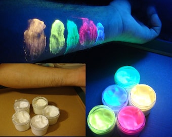 May include: Six small jars of neon glow-in-the-dark paint. The paint is in the colors white, yellow, green, blue, pink, and purple. The jars are arranged in a circle on a dark surface.