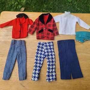May include: A collection of doll clothing including a red blazer with black lapels, a red and black plaid blazer, a white long-sleeve shirt, blue denim pants, blue and white houndstooth patterned pants, solid blue pants, and teal shorts.