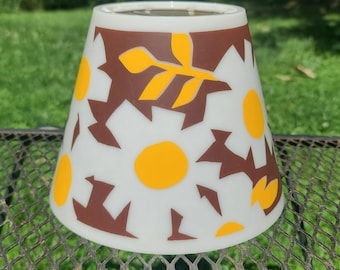 May include: A conical lamp shade featuring a white background with a repeating pattern of dark brown abstract shapes and bright yellow circular and leaf-like motifs. The shade has a smooth, semi-translucent finish and a circular opening at the top.