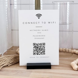 Könnte beinhalten: Ein weißes Schild mit schwarzem Text und einem QR-Code, das für die WLAN-Verbindung bestimmt ist. Auf dem Schild steht "CONNECT TO WIFI" mit dem Netzwerknamen "Silo" und dem Passwort "Snowyowl". Es wird auf einer Holzoberfläche angezeigt.