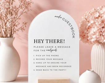 May include: An arched white sign with black text that reads: audio GUESTBOOK, HEY THERE! PLEASE LEAVE A MESSAGE FOR THE newlyweds, 1. PICK UP THE PHONE, 2. RECORD YOUR MESSAGE, 3. HANG UP TO ENSURE YOUR MESSAGE HAS BEEN RECORDED, 4. HEAD BACK TO THE PARTY!
