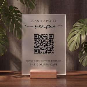 May include: A rectangular frosted acrylic sign featuring black text that reads SCAN TO PAY BY venmo, a central QR code, and the text THANK YOU FOR YOUR BUSINESS THE CORNER CAFÉ at the bottom, all supported by a light-colored wooden base.