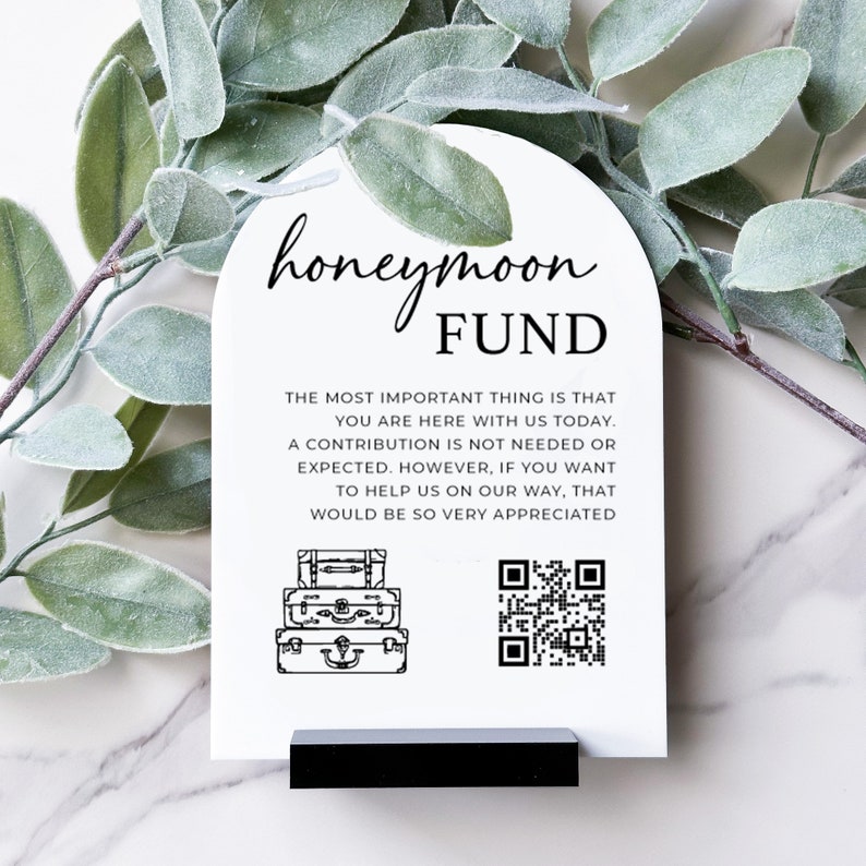 Pu&ograve; includere: Un biglietto bianco con un arco nero in alto che dice "honeymoon FUND". Il testo sotto dice "La cosa pi&ugrave; importante &egrave; che tu sia qui con noi oggi. Un contributo non &egrave; necessario o previsto. Tuttavia, se vuoi aiutarci nel nostro viaggio, sarebbe molto apprezzato". Ci sono tre valigie impilate e un codice QR.