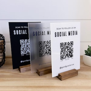 Könnte beinhalten: Drei rechteckige Acrylschilder in Schwarz, Milchglasoptik und Weiß, die jeweils in einem Holzsockel stecken. Die Schilder zeigen den Text SCAN TO FOLLOW US ON SOCIAL MEDIA, einen QR-Code und den Handle @gandgcostarica in fetter Schrift.