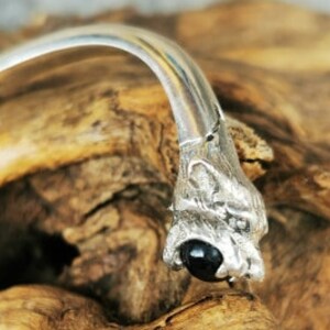 May include: A silver bracelet with two wolf head charms. Each charm has a black gemstone eye.