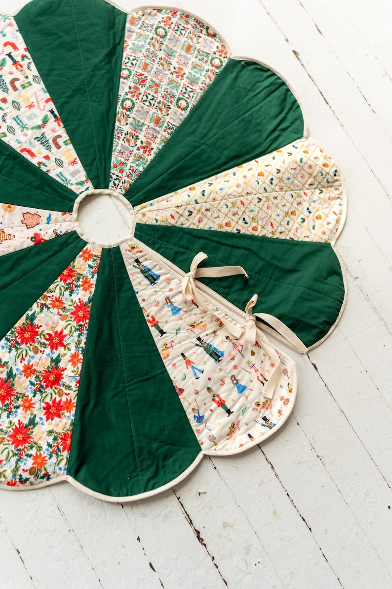 May include: A circular quilted tree skirt with a scalloped edge, featuring alternating panels of solid dark green fabric and cream-colored fabric printed with festive holiday motifs including nutcrackers, poinsettias, and ornaments, secured with cream ties.