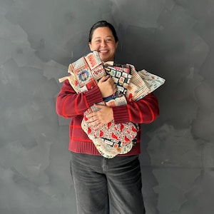 May include: A collection of fabric tote bags featuring various patterns including postage stamps, leopard print, and stripes. The bags are made of cotton and have sturdy handles. The patterns include red, black, and white colors with detailed graphic prints.