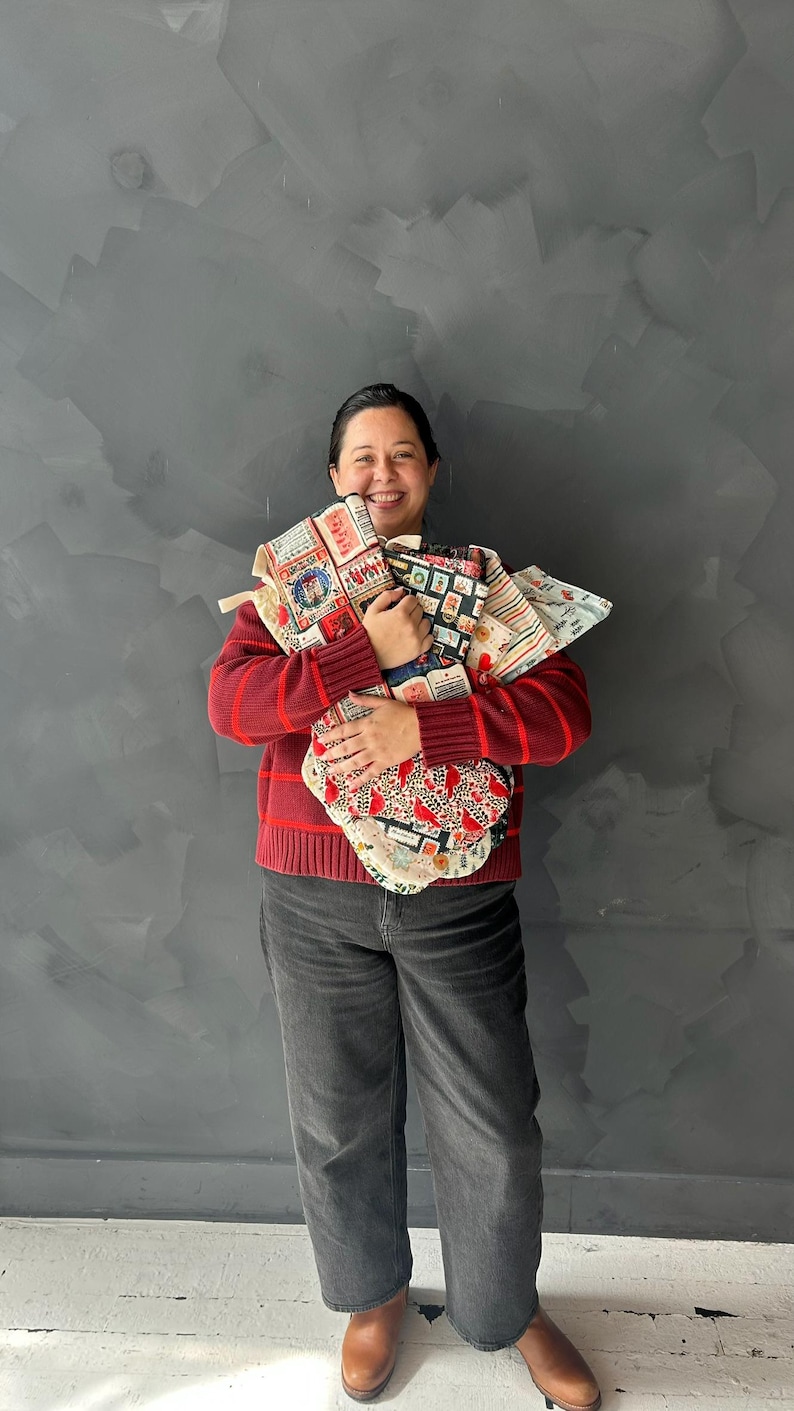 May include: A collection of fabric tote bags featuring various patterns including postage stamps, leopard print, and stripes. The bags are made of cotton and have sturdy handles. The patterns include red, black, and white colors with detailed graphic prints.