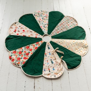 May include: A circular, scalloped-edge tree skirt featuring alternating panels of solid dark green fabric and patterned fabric. The patterns include nutcracker figures, red poinsettias, and festive holiday motifs. It has a center opening and ties.