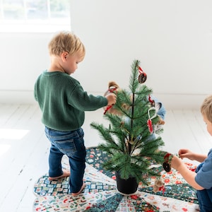 May include: A circular fabric Christmas tree skirt featuring a patchwork design of various holiday-themed patterns including floral motifs, holly leaves, and festive icons in shades of red, green, white, and dark blue with a scalloped edge.