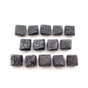 Puede incluir: Una colección de 12 piedras preciosas negras de forma cuadrada dispuestas en tres filas.