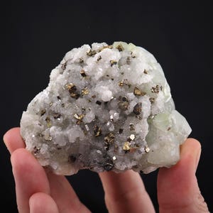 May include: A mineral specimen featuring a cluster of pale green crystals combined with white crystalline structures and small, metallic gold-colored cubic pyrite inclusions scattered across the textured, uneven surface of the rock formation.