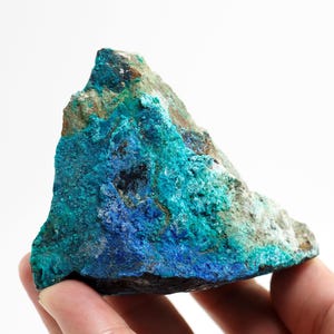 Könnte beinhalten: Ein rohes Mineralexemplar mit einer auffälligen Farbgebung. Der Stein weist eine Mischung aus tiefen Blautönen, leuchtenden Türkistönen und erdfarbenen Brauntönen auf. Die Oberfläche hat ein strukturiertes Aussehen und zeigt die natürliche Formation des Steins.