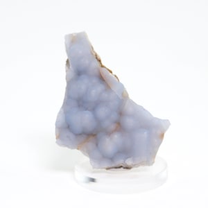 May include: A light blue mineral specimen with a bubbly texture, displayed on a clear, round stand. The mineral has a rough, uneven surface and a mix of light blue and brown colors. The background is white.