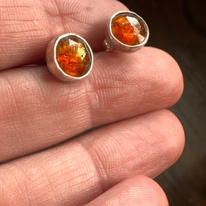 Puede incluir: Un par de pendientes de plata con piedras redondas de color marr&oacute;n anaranjado. Las piedras tienen una calidad brillante e iridiscente.