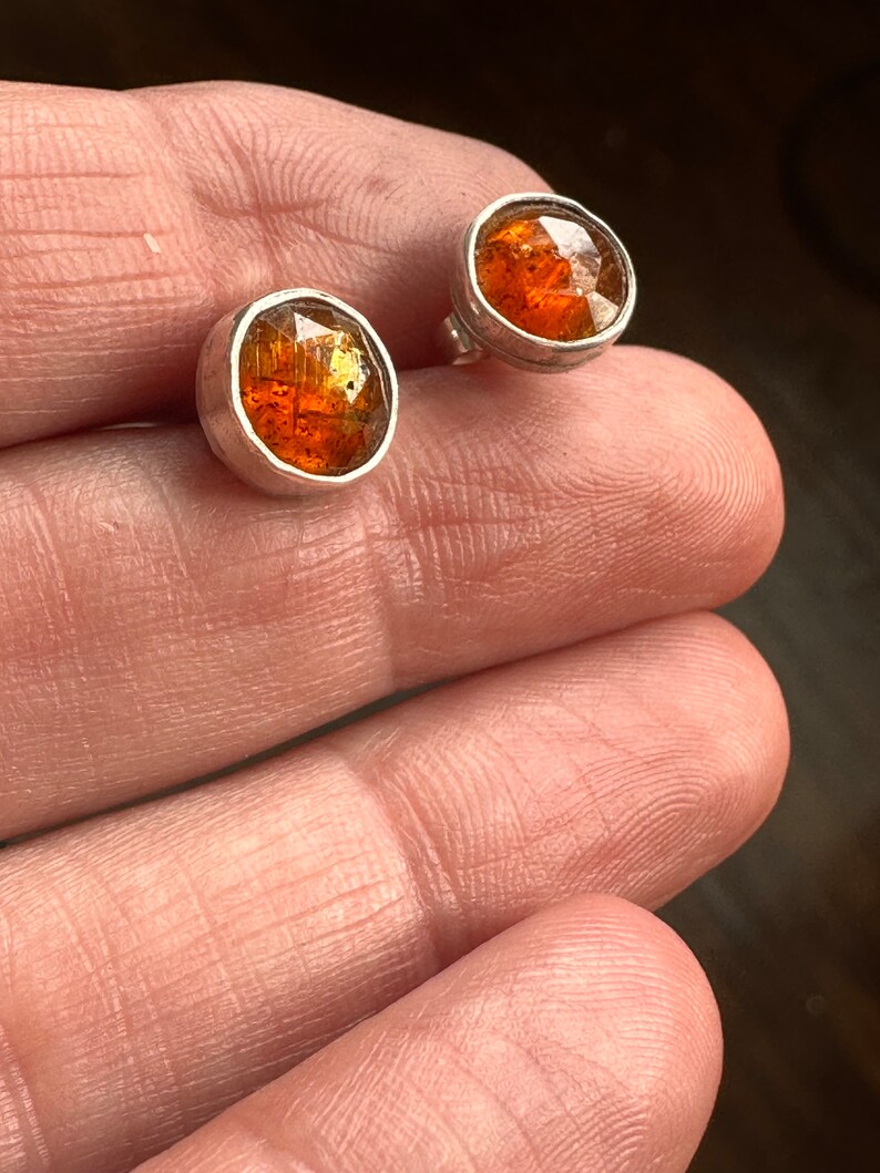 Puede incluir: Un par de pendientes de plata con piedras redondas de color marr&oacute;n anaranjado. Las piedras tienen una calidad brillante e iridiscente.