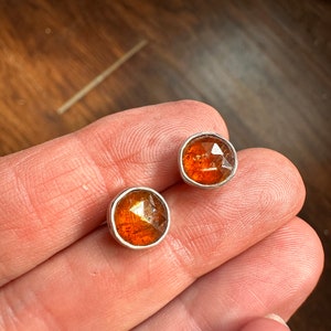 Puede incluir: Un par de pendientes de plata con detalles de piedras preciosas naranjas. Las piedras preciosas son facetadas y tienen una forma ligeramente irregular.
