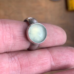 May include: A silver ring with a round, pale green gemstone set in the center.