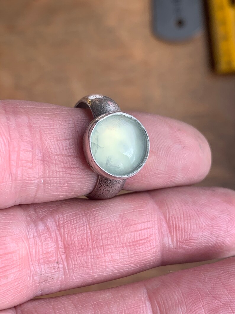 May include: A silver ring with a round, pale green gemstone set in the center.