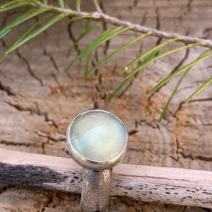 May include: A silver ring with a light green gemstone. The ring has a textured band.