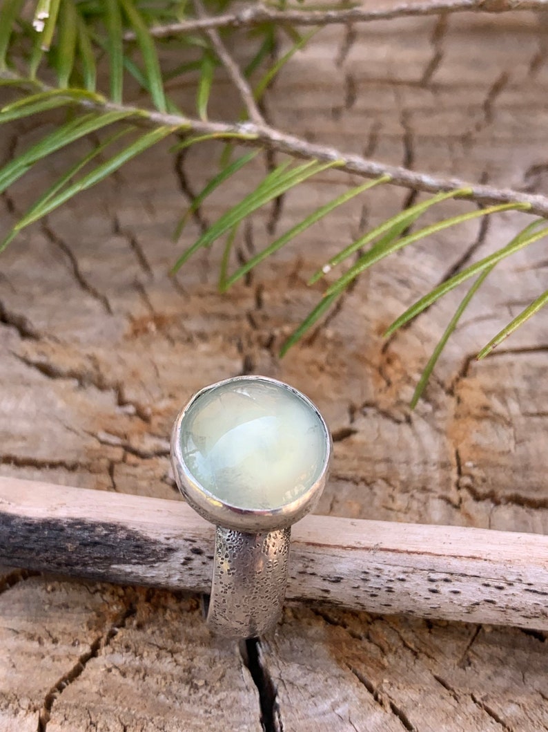 May include: A silver ring with a light green gemstone. The ring has a textured band.