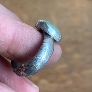 May include: A silver ring with a textured band and a light green oval gemstone.