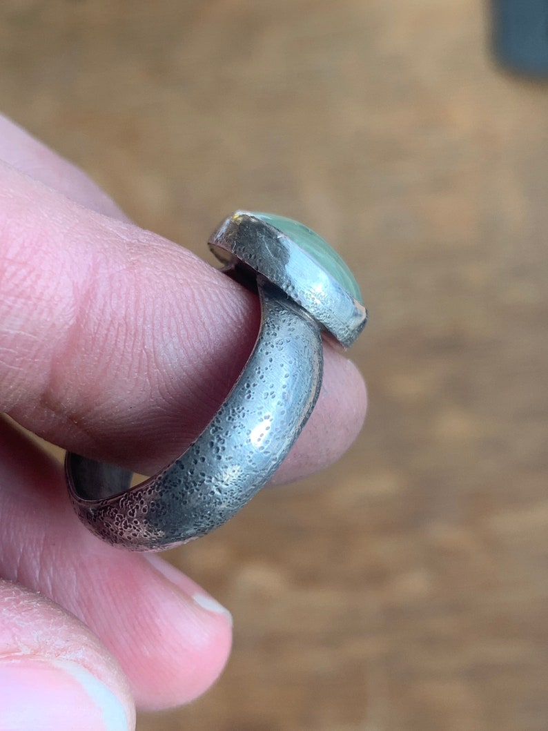 May include: A silver ring with a textured band and a light green oval gemstone.