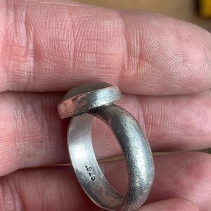 May include: A silver ring with a textured band and a round, smooth gemstone. The ring is stamped with the number "925" on the inside of the band.