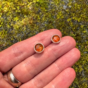 Puede incluir: Un par de pendientes de bot&oacute;n de plata con piedras redondas de color naranja.