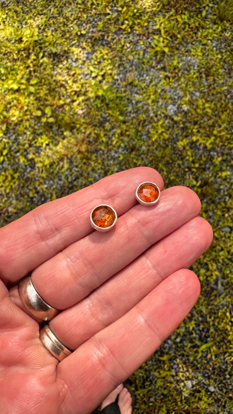Puede incluir: Un par de pendientes de bot&oacute;n de plata con piedras redondas de color naranja.