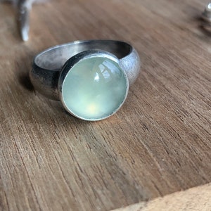May include: A silver ring with a light green gemstone set in a bezel setting.