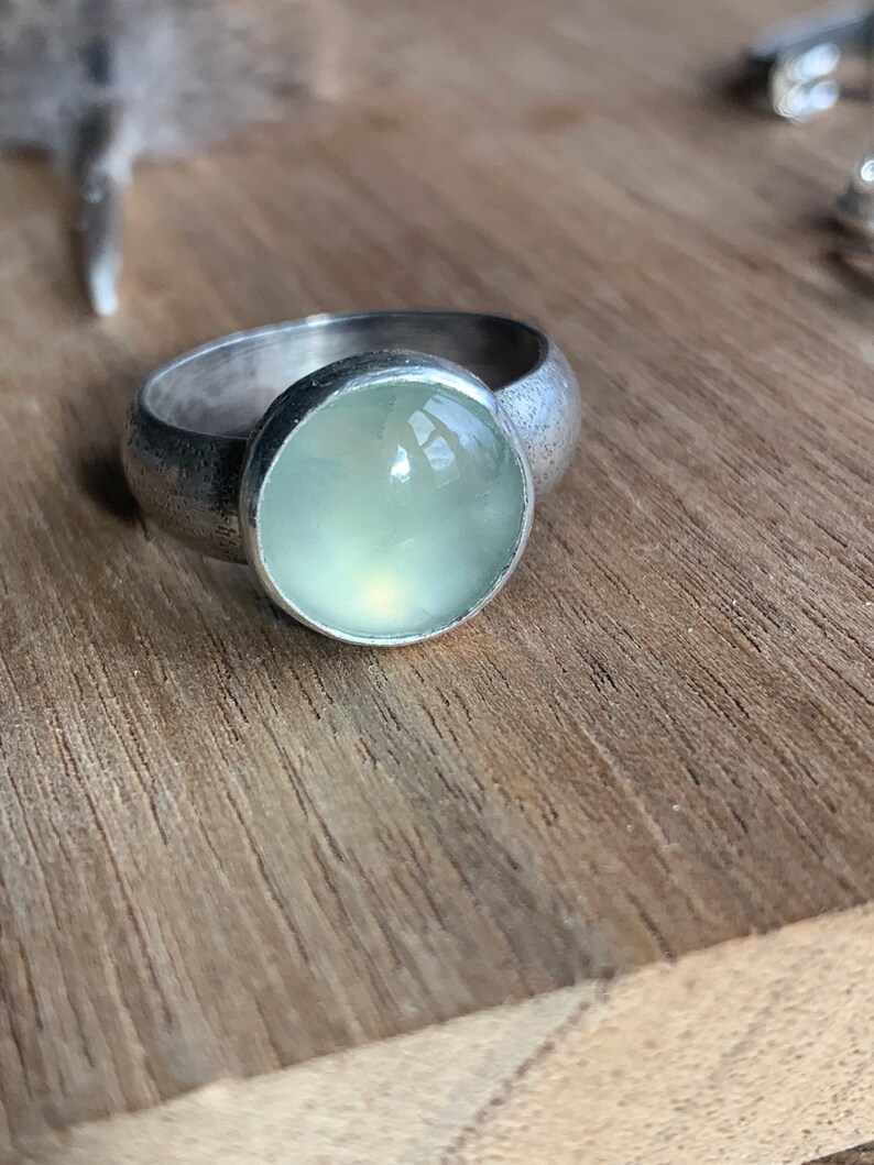 May include: A silver ring with a light green gemstone set in a bezel setting.