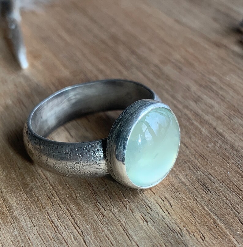 May include: A silver ring with a textured band and a light green gemstone.