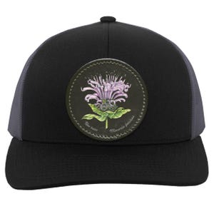 Puede incluir: Gorra de camionero negra con un parche redondo de cuero negro que presenta una flor de bálsamo de abeja púrpura y verde con el texto "Bee balm Monarda fistulosa".