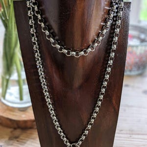 May include: A silver chain necklace with a T-bar clasp. The necklace is layered with two chains of different lengths.