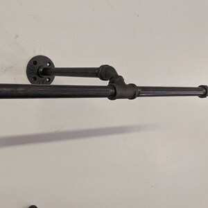 K&ouml;nnte beinhalten: Schwarzer Metall-Handtuchhalter an einer wei&szlig;en Wand montiert. Der Halter hat zwei horizontale Stangen und eine vertikale St&uuml;tze.