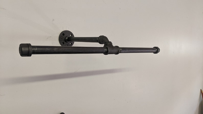 K&ouml;nnte beinhalten: Schwarzer Metall-Handtuchhalter an einer wei&szlig;en Wand montiert. Der Halter hat zwei horizontale Stangen und eine vertikale St&uuml;tze.