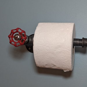 May include: A red industrial-style toilet paper holder with a black pipe and a red valve handle. The holder is mounted to a light blue wall.