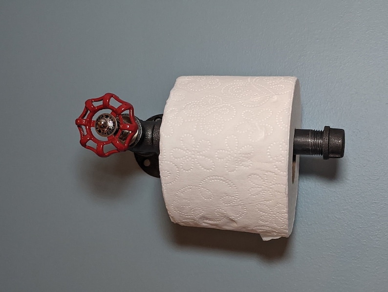 May include: A red industrial-style toilet paper holder with a black pipe and a red valve handle. The holder is mounted to a light blue wall.