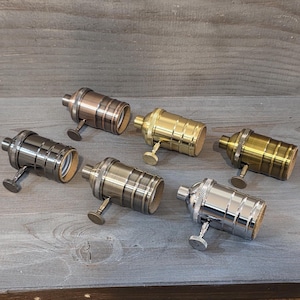 May include: A collection of six vintage-style light bulb sockets in various metallic finishes, including bronze, brass, and silver. Each socket has a small, round knob and a cylindrical design, perfect for DIY lighting projects.