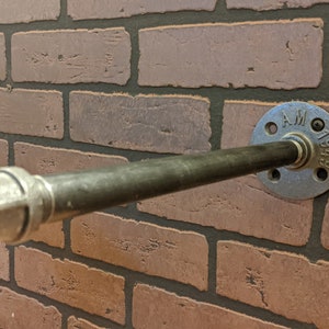 May include: A silver metal pipe shelf bracket with a black pipe attached. The bracket has the text "AM 1940" on it.