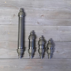 May include: Four industrial-style metal pipe fittings of varying sizes. The largest is a tall, cylindrical piece, while the others are shorter and more compact. All have a threaded base and a cap on top. The fittings are made of a dark gray metal.